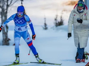 Slovenská biatlonistka na trati v Pekingu 2022, vpravo muž v bunde slovenskej výpravy.